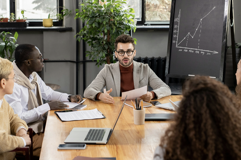 Cuatro personas reunidas en una sala con un ordenador portátil, papeles, bolígrafos y una pizarra.