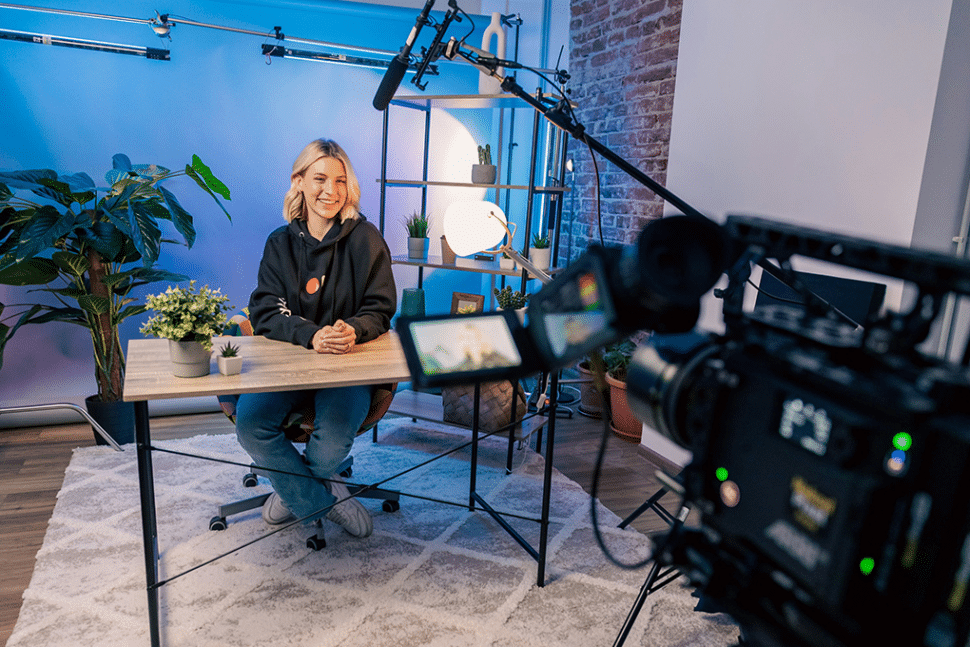 A woman sits at a table in front of a video camera and microphone, recording a transcription