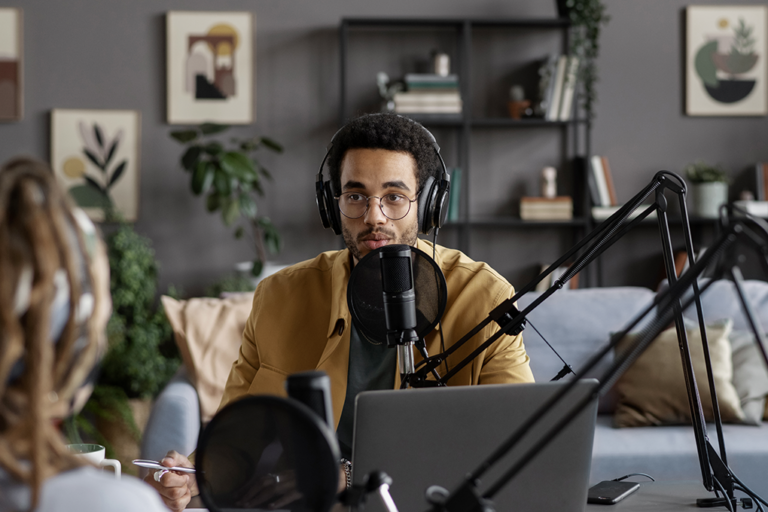 A man is transcribing using headphones, a laptop, and a microphone