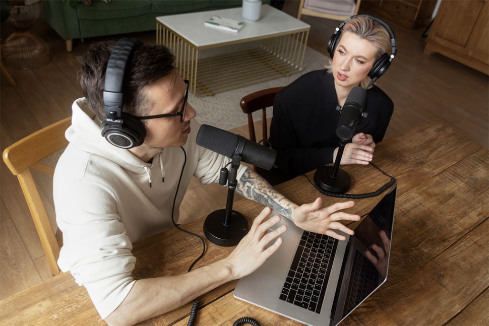 Ein Mann und eine Frau, die mit einem Mikrofon, Kopfhörern und einem Laptop Tonaufnahmen machen