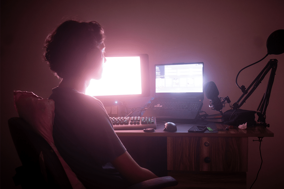 Eine Frau sitzt vor einem Computer, einem Laptop und einem Mikrofon und arbeitet an einer Transkriptionsaufgabe