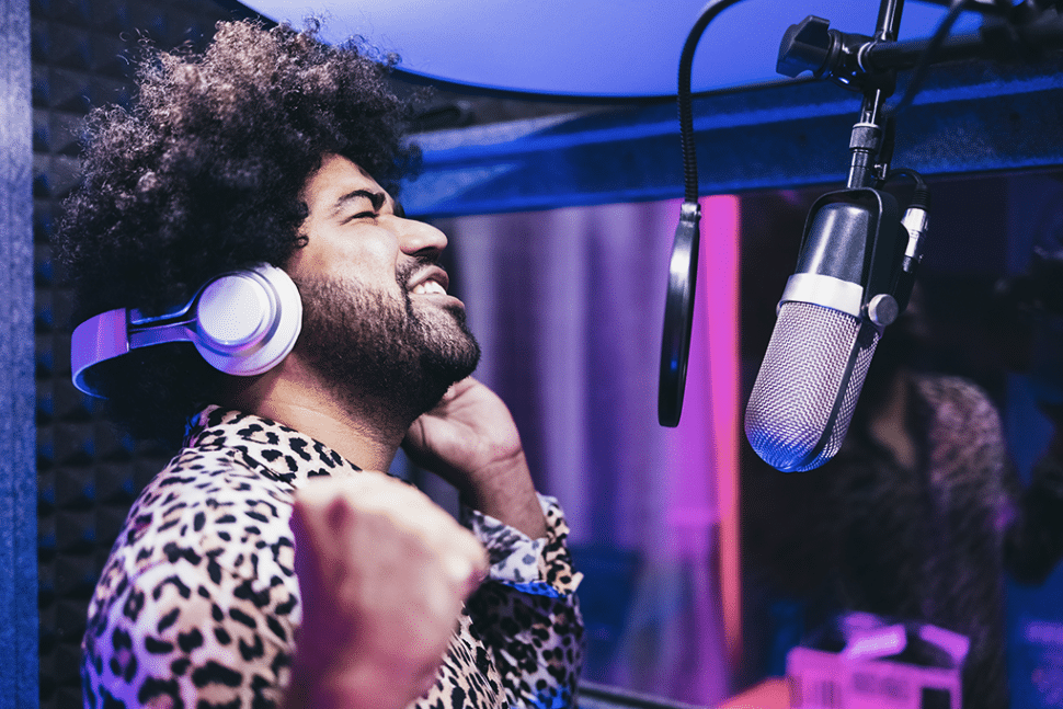 A man is transcribing in a room, using a microphone, a vocal filter, and headphones