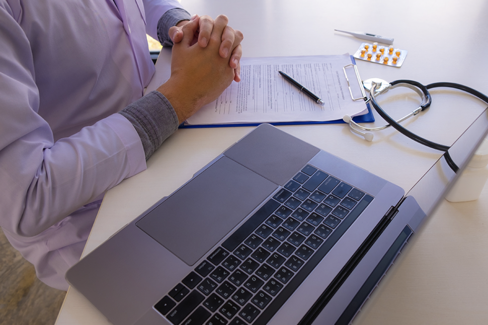doctors handing interlinked in front of a laptop with a notepad