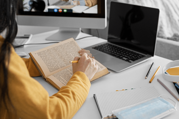 Frau, die vor ihrem Computer Notizen aus einem Buch macht