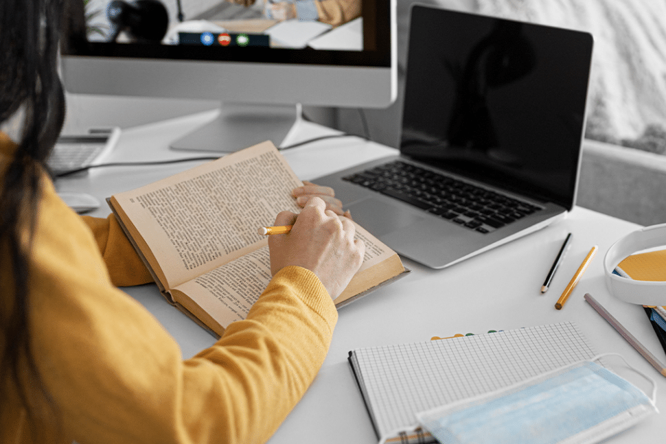 bilgisayarının önünde kitaptan notlar alan kadın