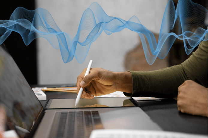 Hand tippt auf einem Tablet, während sie eine Datei auf ihrem Laptop anhört