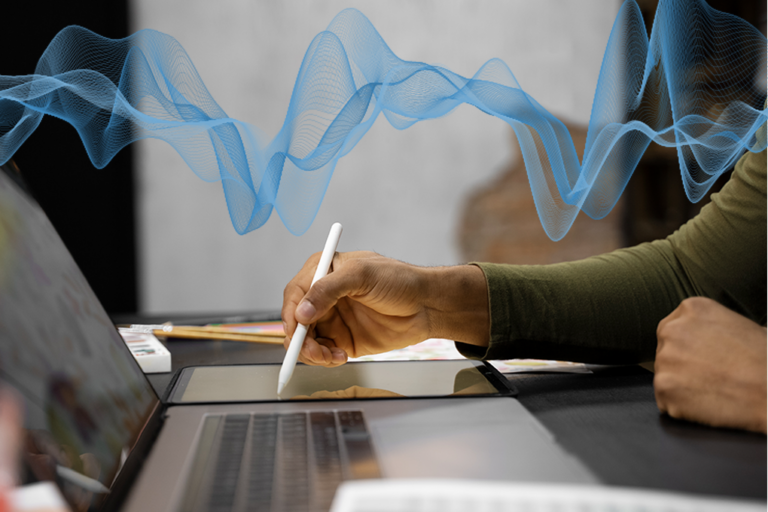 hånd, der skriver på en tablet, mens hun lytter til en fil på sin bærbare computer